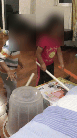 Two children drumming energetically on an upturned bucket — inventive, high-energy play