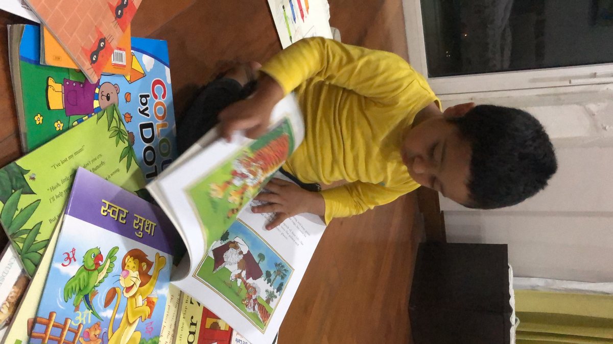 A boy surrounded by open picture books, including a Hindi alphabet book, absorbed in the one on his lap