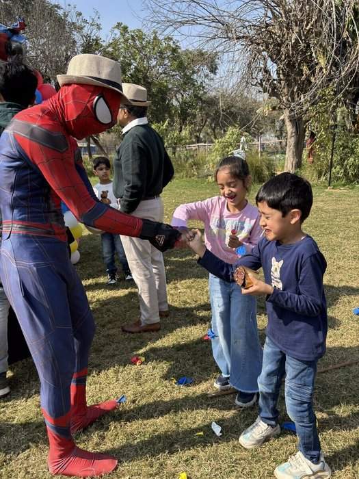 एक बाहरी आयोजन में बच्चे — एक लड़की और एक लड़का — किसी costume वाले किरदार से खुश होकर मिल रहे हैं