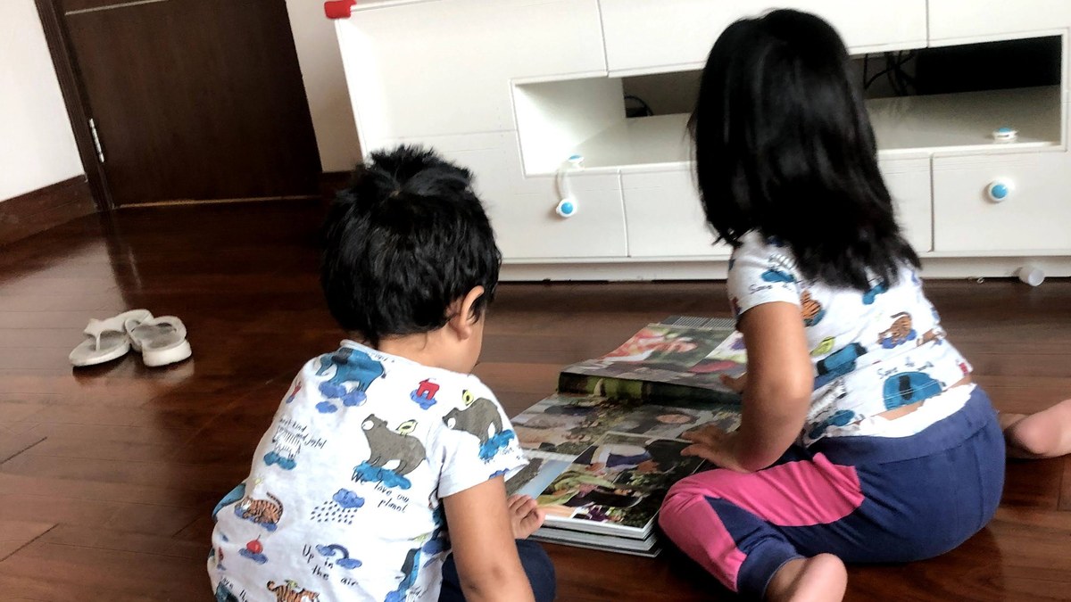 Two young children sitting on the floor at home, leaning over a large photo book together