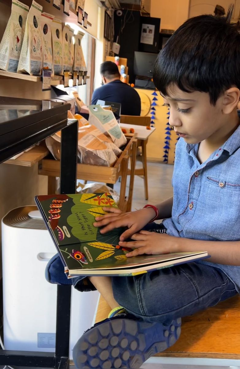 A boy sitting cross-legged on a bench in a bookshop café, absorbed in an illustrated book