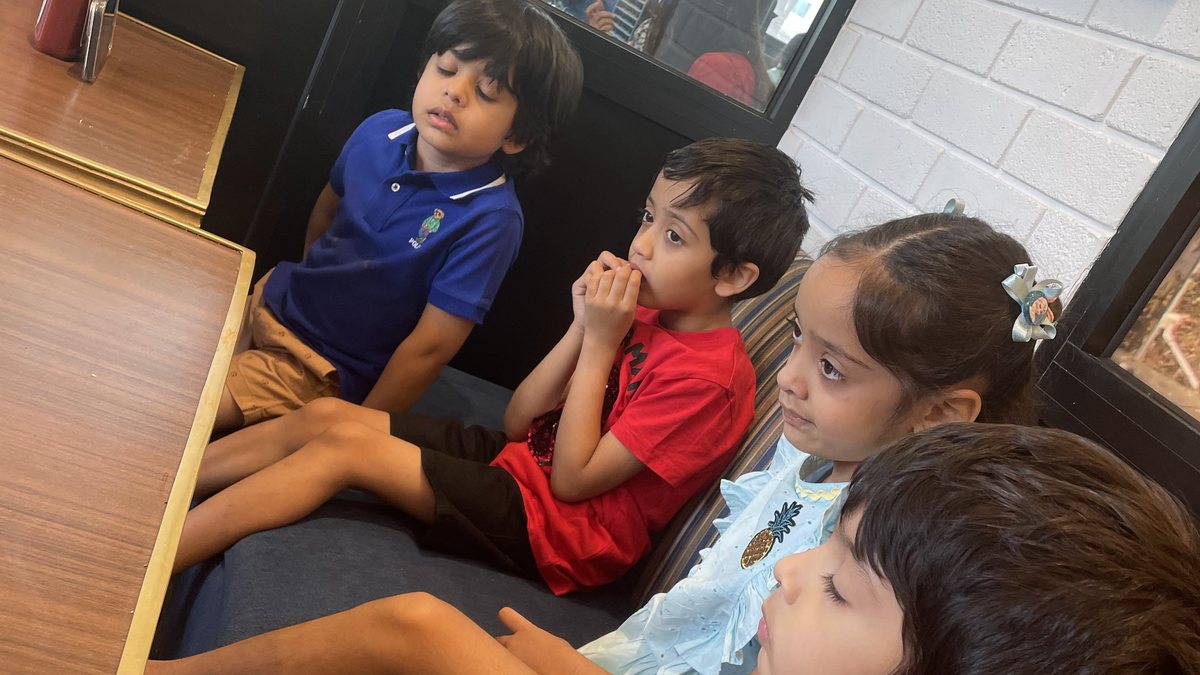 Four children sitting in a row on a café bench, waiting, none of them occupied