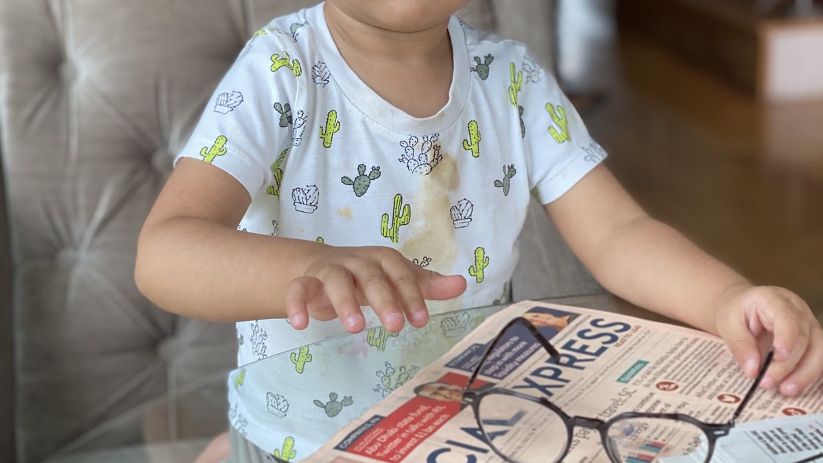 A small child's hands resting on a financial newspaper, next to a pair of adult reading glasses